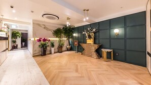 A hotel lobby with a marble reception desk, wooden flooring, green paneling, and potted plants.