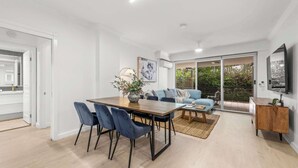 A modern living space with a dining area, sofa, and a TV. - Spacious 3BR Retreat | Pool, Gym & Parking (Bowen Hills)