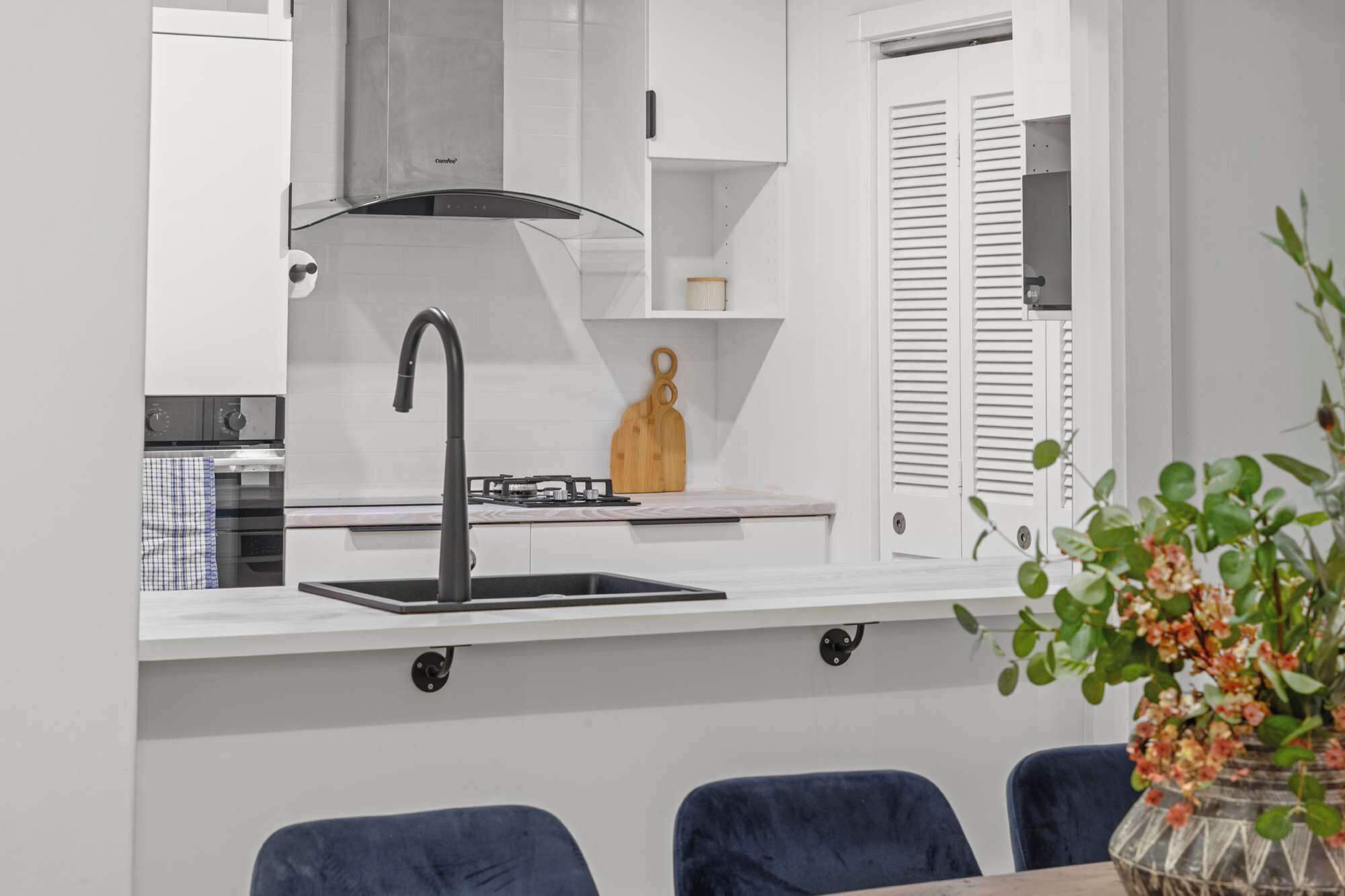 A modern kitchen with a stainless steel range hood, a black faucet, and a wooden cutting board on the countertop.