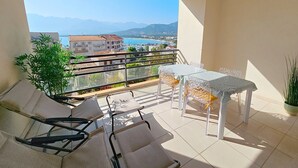 Un balcon avec une table et des chaises, un pot de fleurs et une vue sur des immeubles et des montagnes.
