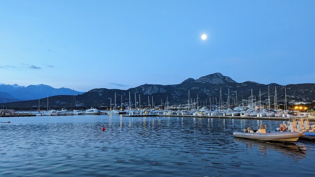 Un port de plaisance avec des bateaux amarrés, une eau calme et des montagnes en arrière-plan.