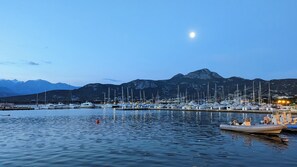 Uma marina com barcos atracados, água calma e montanhas ao fundo.