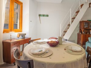Un coin repas avec une table ronde dressée pour quatre personnes, une machine à coudre, un meuble en bois et un escalier.
