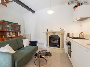 A compact living space with a green sofa, a small round table, a fireplace, and a kitchen area. - La Giuseppina by Interhome (Brovello Carpugnino)