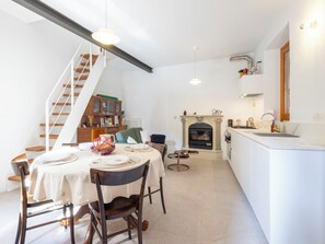 A modern kitchen with a fireplace, a dining area with a table set for four, and a staircase leading to an upper level. - La Giuseppina by Interhome (Brovello Carpugnino)