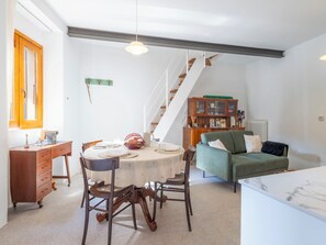 Un coin repas avec une table dressée pour quatre personnes, un meuble en bois, un canapé vert et un escalier.