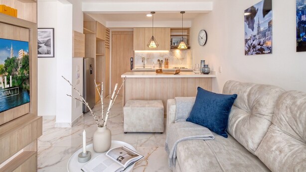 A modern living room with a sofa, a coffee table with a magazine, a vase with branches, and a TV on the left. - Edificio Miro Guadalupe (Cali)