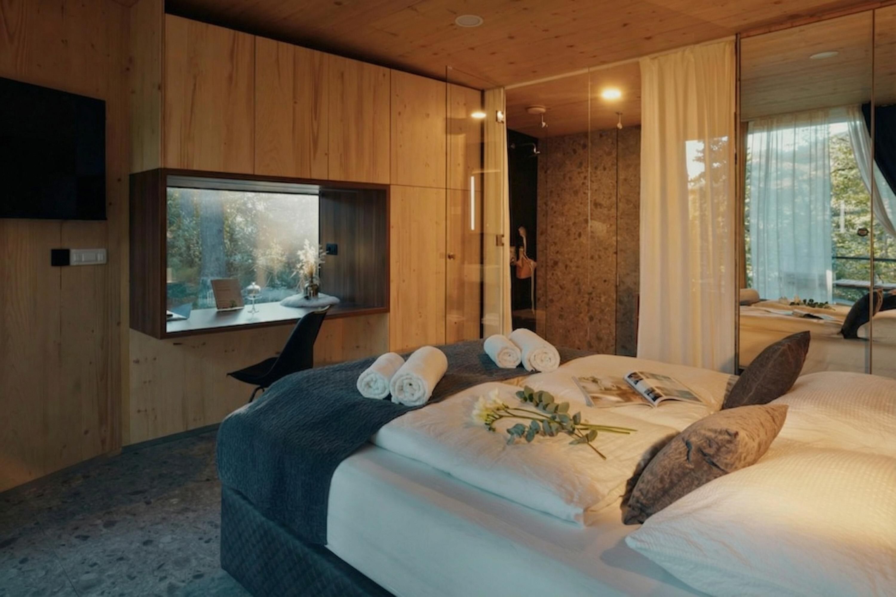 Ein modernes Schlafzimmer mit einem großen Bett, einem an der Wand montierten Fernseher und Blick ins Freie.