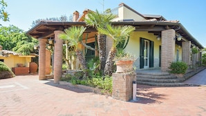 Een gebouw in mediterrane stijl met een bakstenen gevel, een overdekte veranda met zuilen en een aangelegde entree.