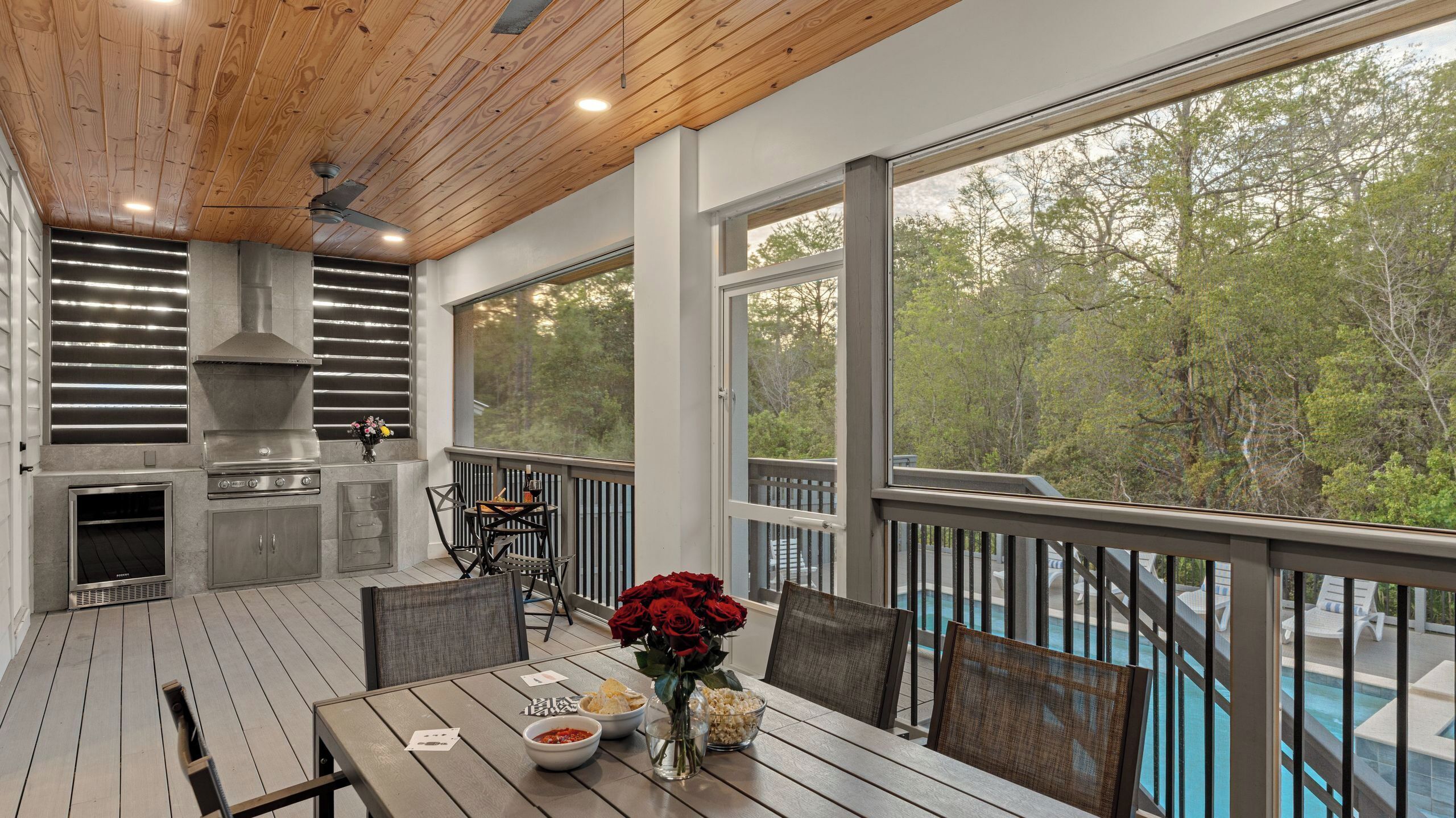 Une terrasse extérieure avec une table à manger, des chaises, un barbecue et une vue sur une piscine.