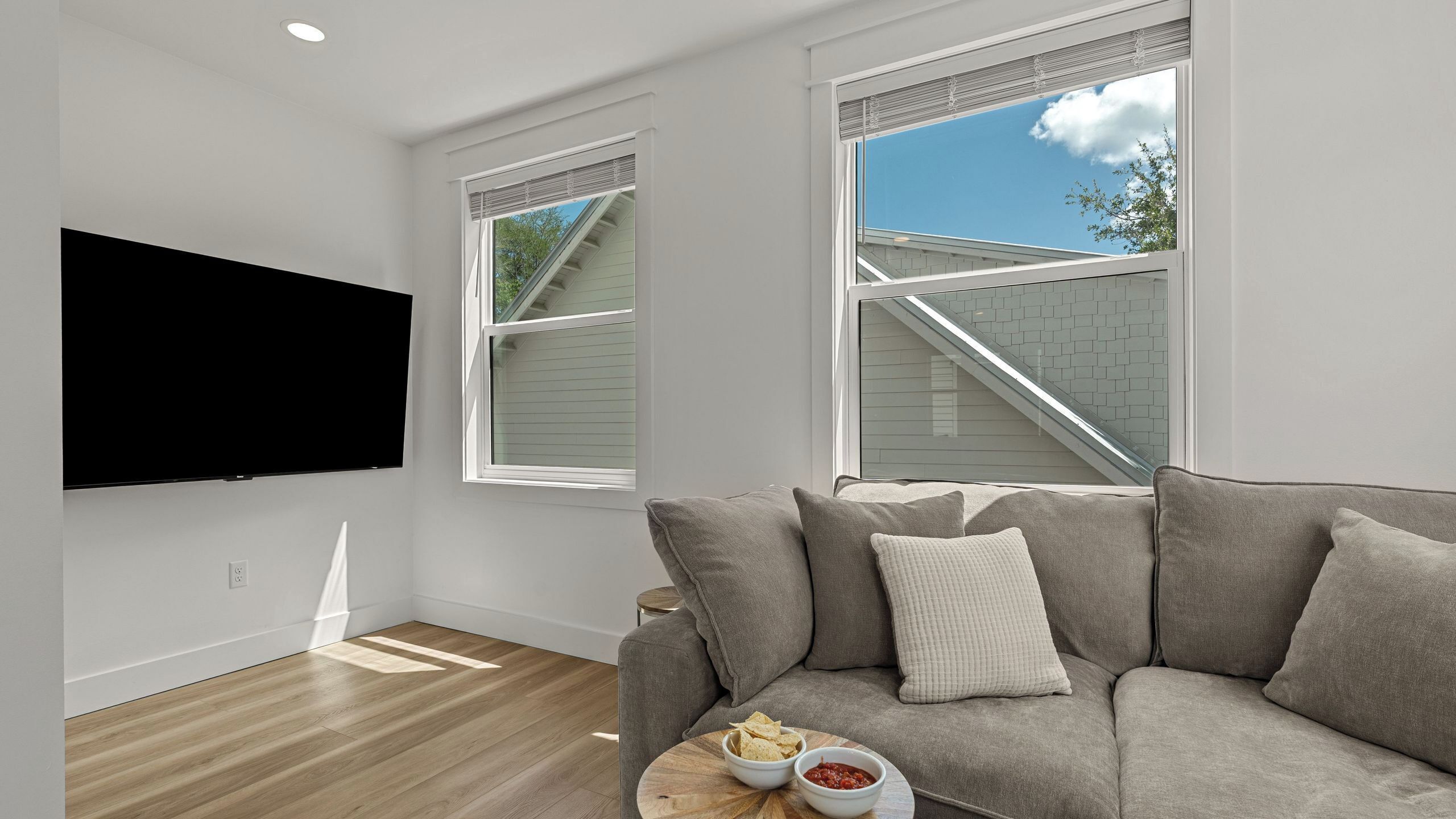 A modern living room with a flat-screen TV, a grey sofa, and a wooden coffee table with snacks.