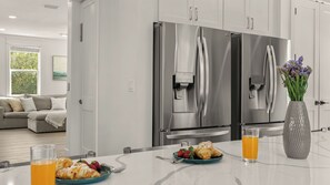 Eine moderne Küche mit Edelstahlgeräten, ein Essbereich mit einem für das Frühstück gedecktem Tisch und ein Wohnzimmer mit einer Couch und einem Gemälde.