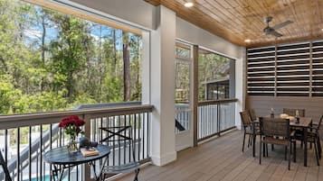 Un espace extérieur abrité, doté d’une table et de chaises, de grandes fenêtres et offrant une vue sur les arbres.