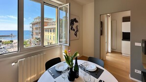 A dining area with a table set for two, a view of the sea and buildings, and a door leading to another room. - Double One Beach & City (Recco)