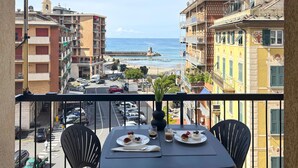 A balcony with a table set for two, overlooking a coastal street with buildings and a pier. - Double One Beach & City (Recco)