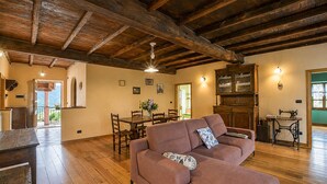 A cozy living room with a wooden ceiling, a sofa, a dining table, and a sewing machine.