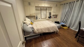 A bedroom with a bed, a ceiling fan, built-in cabinets, a window with curtains, and a wooden floor. - Heart of Houston five bedroom near everything (Houston)