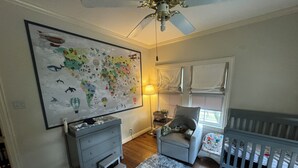 A child's room with a world map, a crib, a chair, and a small table with a lamp. - Heart of Houston five bedroom near everything (Houston)