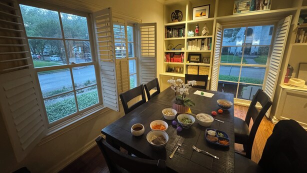 A dining room with a table set for a meal, surrounded by bookshelves and a view of the street. - Heart of Houston five bedroom near everything (Houston)
