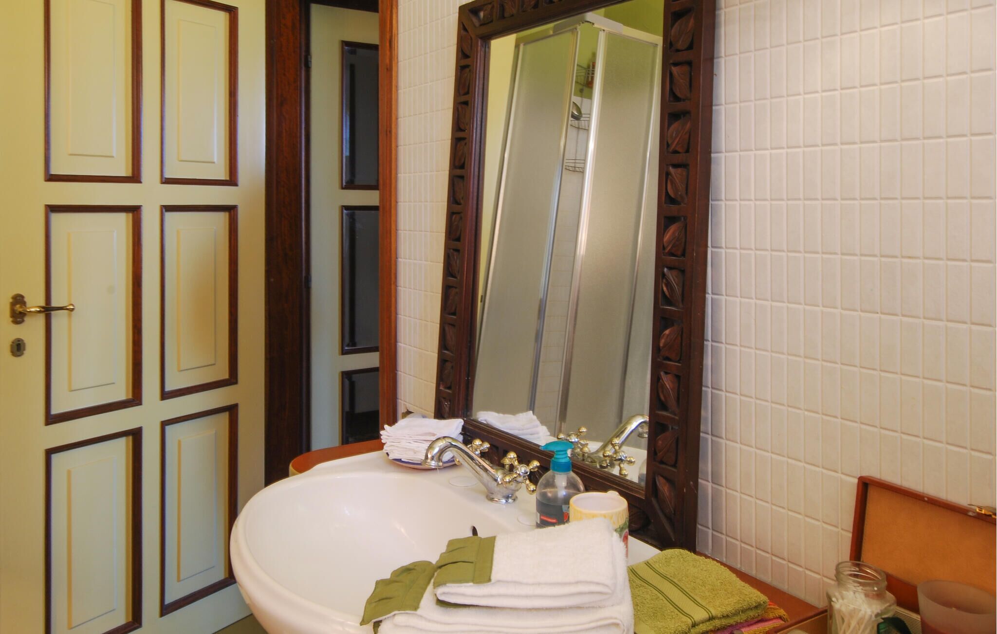 A bathroom with a large mirror, a sink with toiletries, and a towel rack.