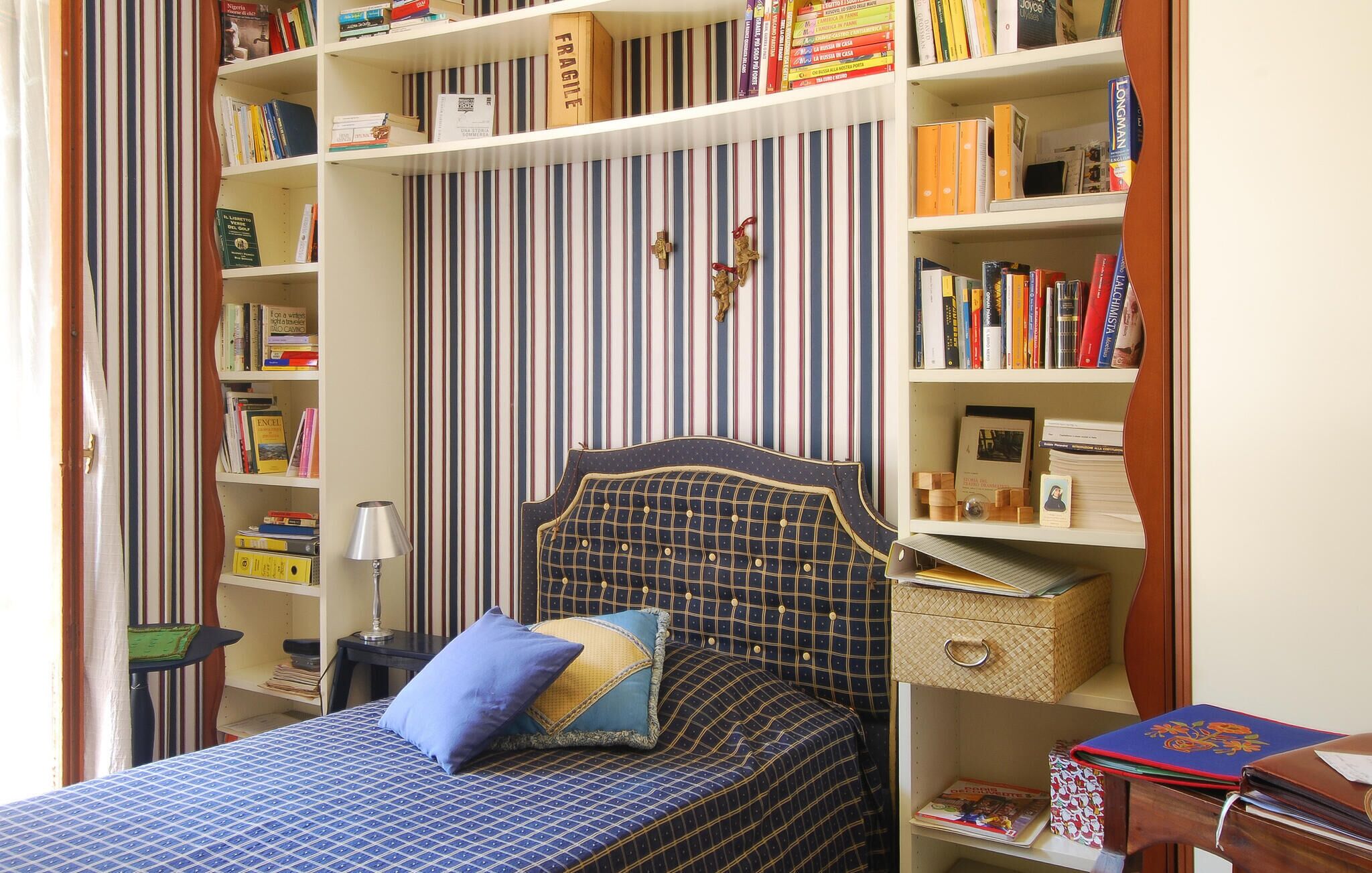 A bedroom with a bed, a bookshelf, a desk, and a striped curtain.