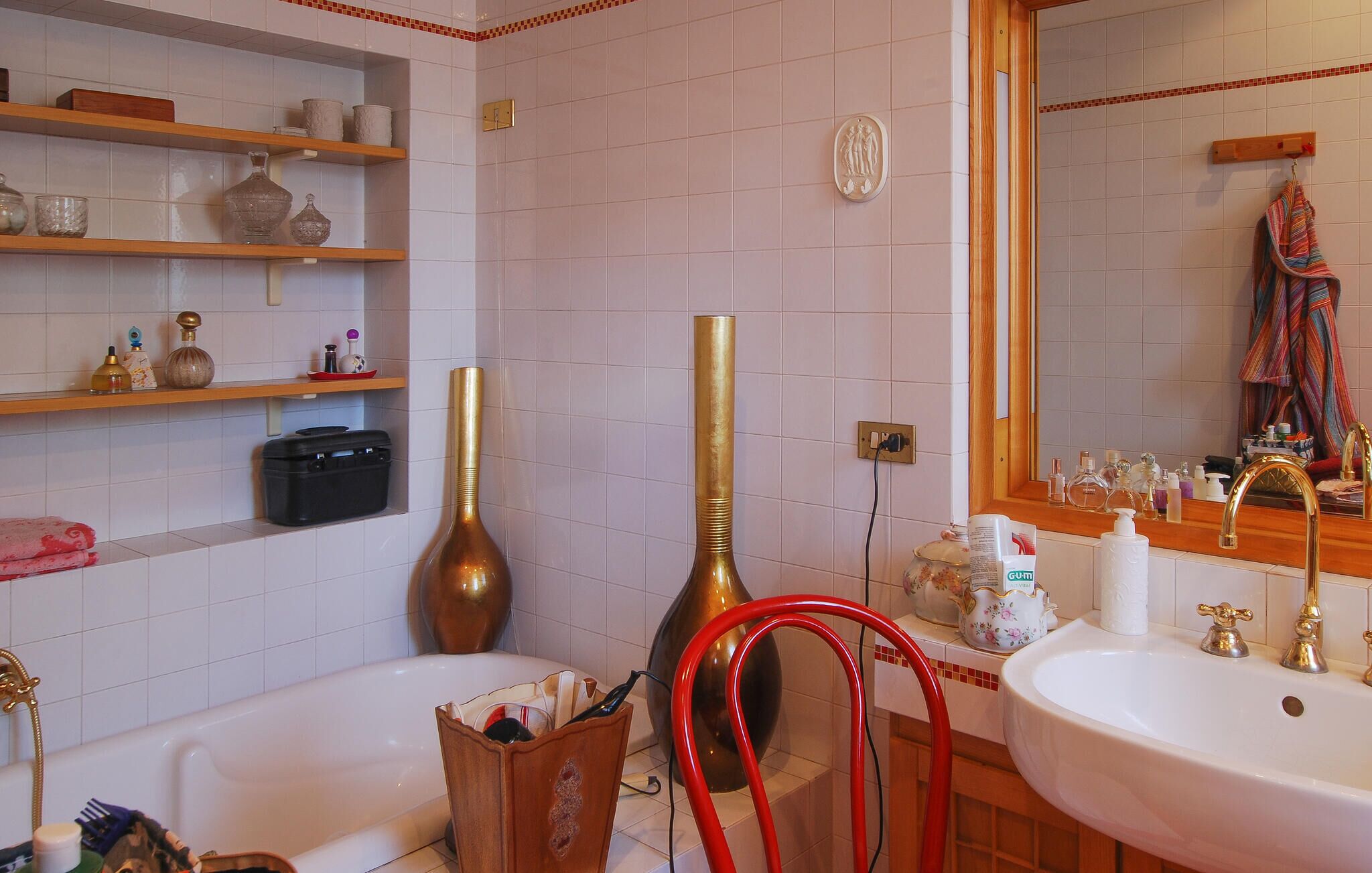 A bathroom with a bathtub, two sinks, a mirror, and shelves with toiletries.