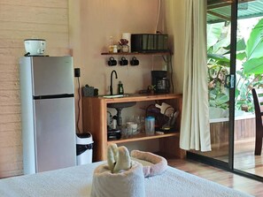 A compact kitchen with a refrigerator, coffee maker, and a sink. There is a small shelf with mugs and a window with a view of greenery. - Cabaña Eden Paradise, nature to relax listening to the birds. (Provincia de Alajuela)