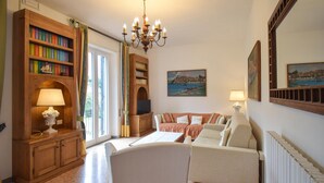 Ein Wohnzimmer mit Sofa, Fernseher, Bücherregal, einer Chandelüster und einem Gemälde.