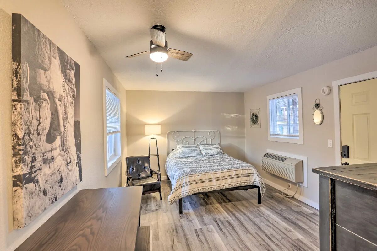A bedroom with a bed, a chair, a ceiling fan, a radiator, and a large painting on the wall.