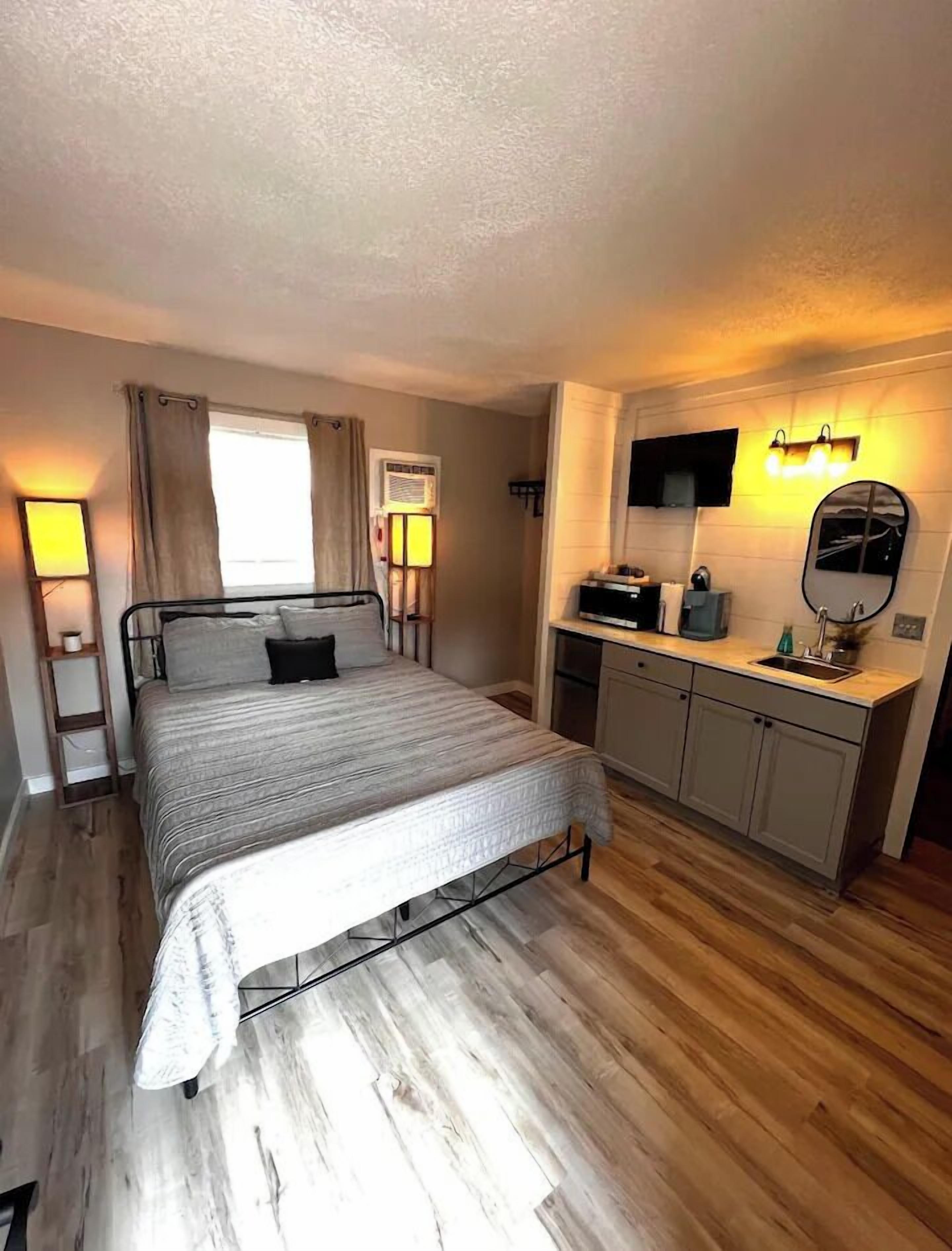 A bedroom with a bed, bedside tables, a desk, a mirror, and a window with curtains.