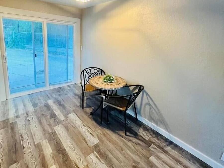 Una habitación con piso de madera, una mesa redonda con sillas, una lámpara en el techo y una puerta corrediza de vidrio que da al exterior.
