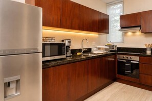 A modern kitchen with stainless steel appliances, wooden cabinets, a built-in oven, and a water dispenser. - Luxury Tropical PH Private Pool (Tulum)