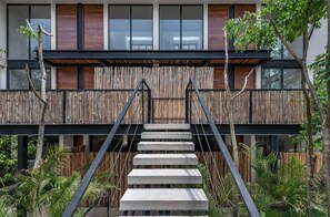 Un bâtiment moderne doté d’une façade en bois, d’un escalier en béton et entouré de verdure.