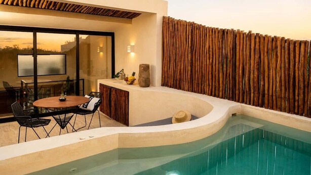 Zona de piscina exterior moderna amb vora corba, taula de menjador amb caires i tanca de fusta.