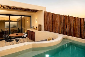 Uma área de piscina moderna ao ar livre, com borda curva, mesa de jantar com cadeiras e cerca de madeira.