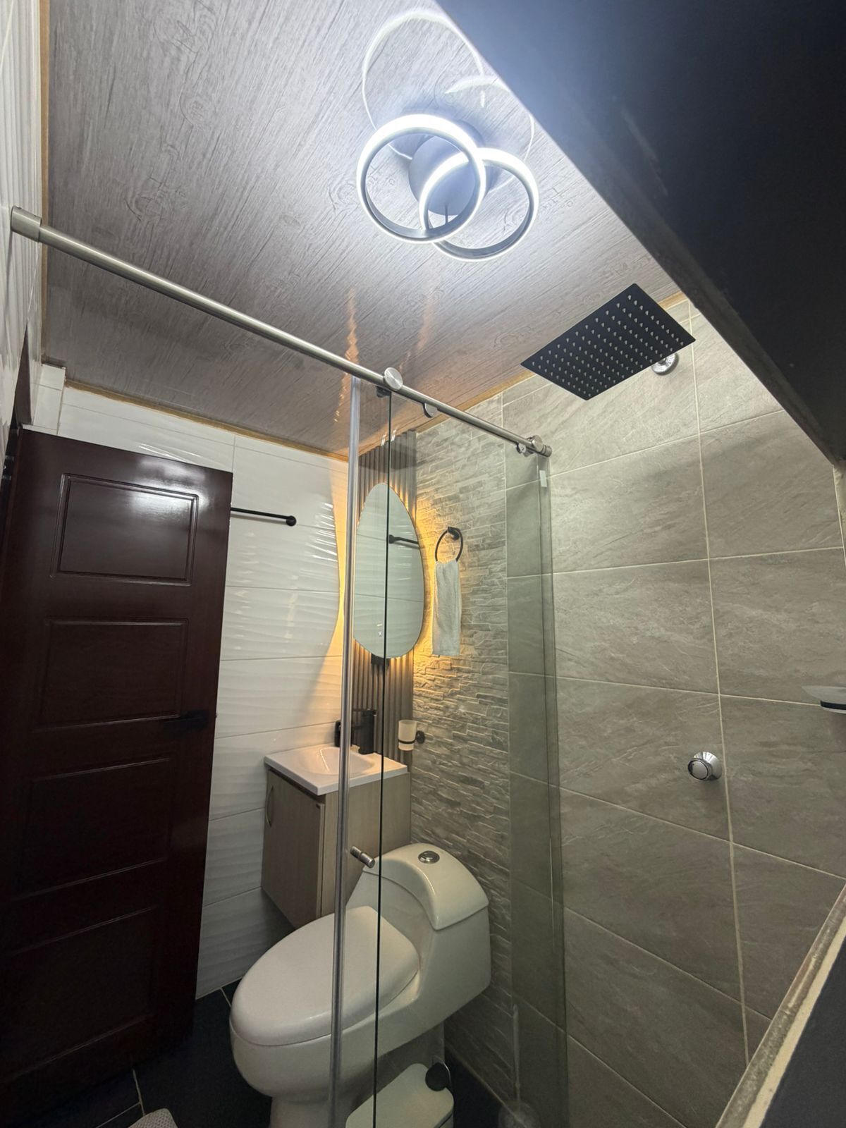 Un bagno moderno con cabina doccia in vetro, un water e un mobile lavabo con specchio.