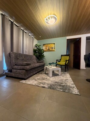 Ein Wohnzimmer mit Sofa, Couchtisch, Sessel, Pflanze und einem Bild an der Wand.