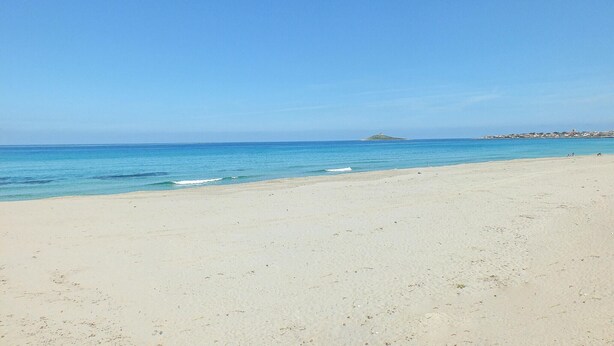 Ein Strand mit klarem, blauem Wasser, einem sandigen Ufer und einer entfernten Insel.