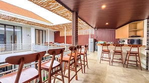 A restaurant with high tables and chairs, a kitchen area, and a balcony with a railing. - Agung Guest House Canggu (Canggu)