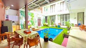 A spacious indoor area with a pool, dining table, chairs, and a kitchen area.