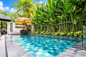 Una piscina con borde de azulejos, rodeada de exuberante vegetación y un área de descanso cubierta.