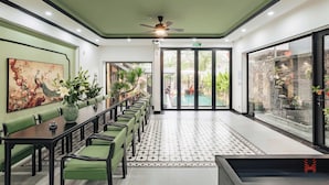 Una sala de conferencias con una larga mesa, sillas verdes, un ventilador de techo y un amplio ventanal con vista a una piscina al aire libre.