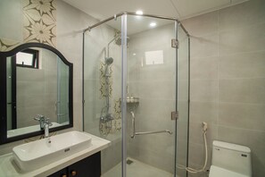 Un baño moderno con ducha envuelta en vidrio, un lavabo blanco y un espejo grande.