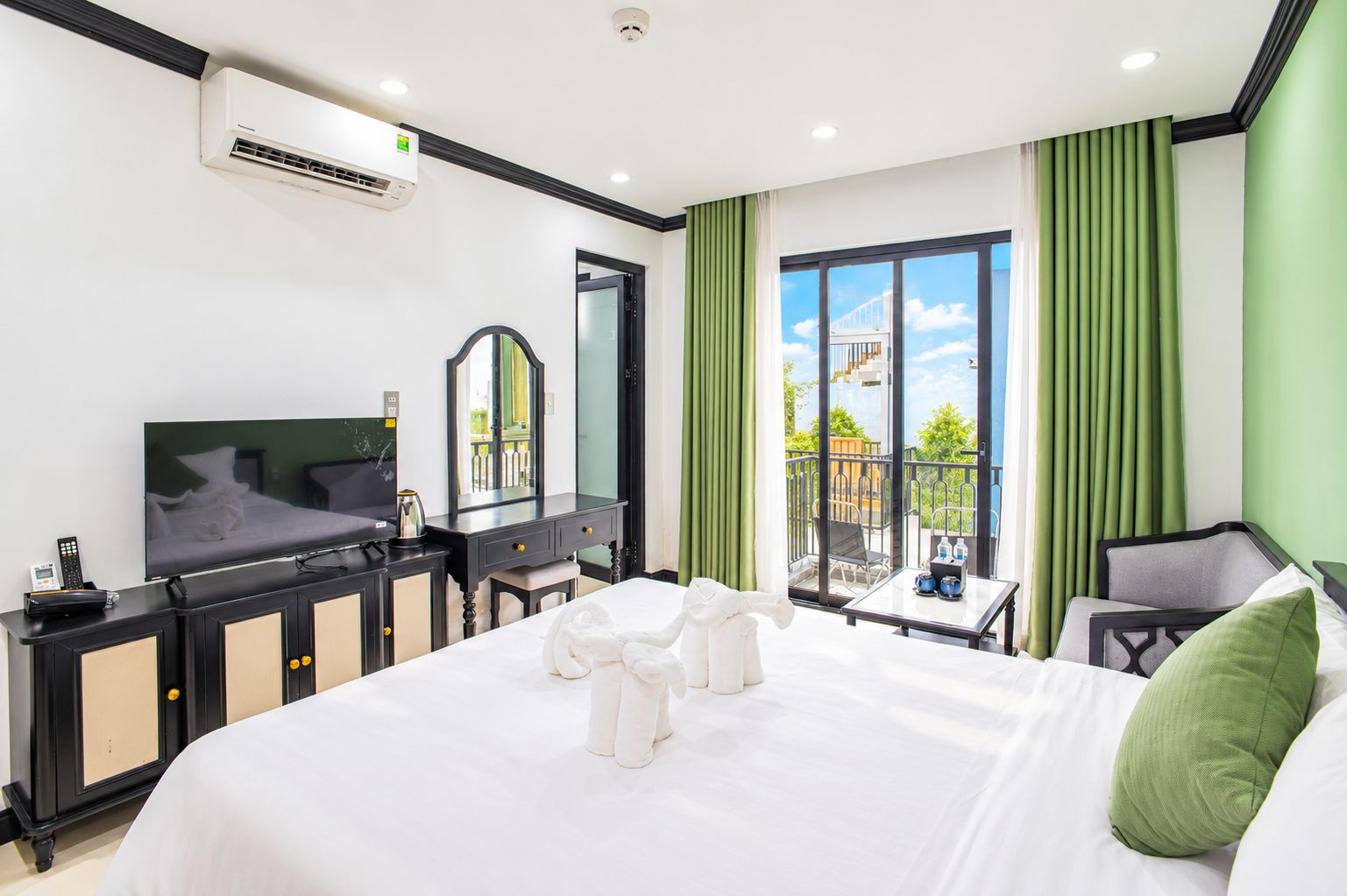 Habitación de hotel con una cama grande, televisión, escritorio con espejo y balcón con vistas.