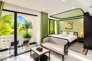 Habitación de hotel con cama, sofá, una mesita, una mesita de noche, lámpara, un cuadro y vistas a zonas verdes.