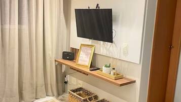 Une pièce avec un téléviseur fixé au mur, une étagère sur laquelle est posé un certificat encadré, une petite plante et des paniers en osier.