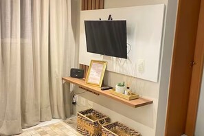 A room with a mounted TV, a shelf with a framed certificate, a small plant, and wicker baskets.
