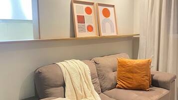 A living room with a sofa, a throw blanket, and two framed artworks on the wall.