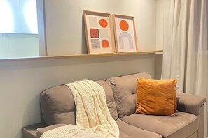 A living room with a sofa, a throw blanket, and two framed artworks on the wall.