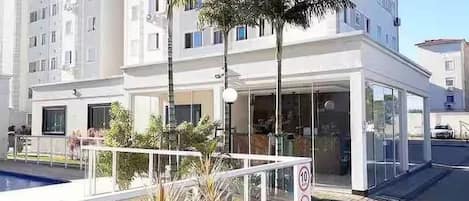 A modern building with a swimming pool, palm trees, and a gated entrance.
